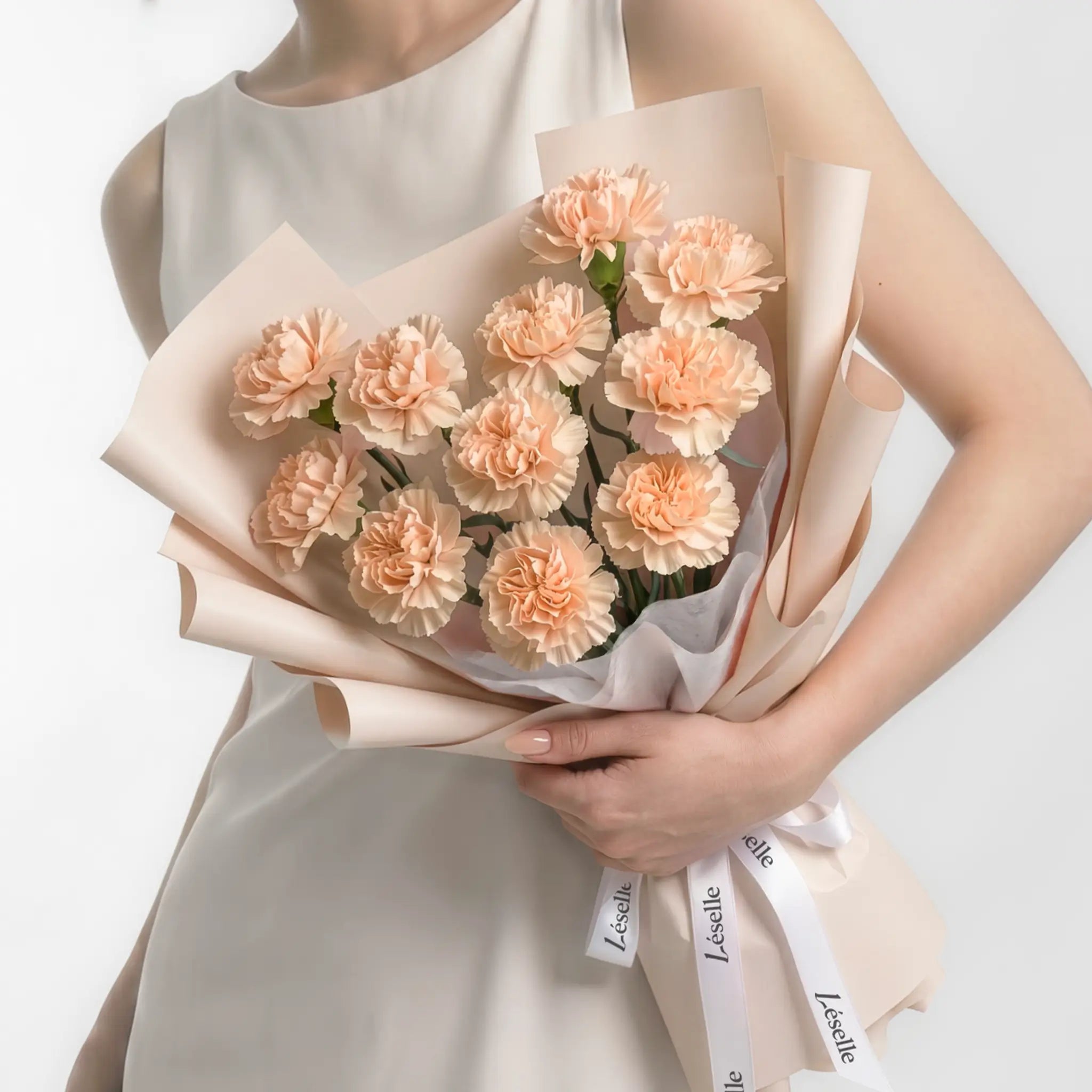 Bouquet of peach pink carnations held by a person in a white dress on a white background