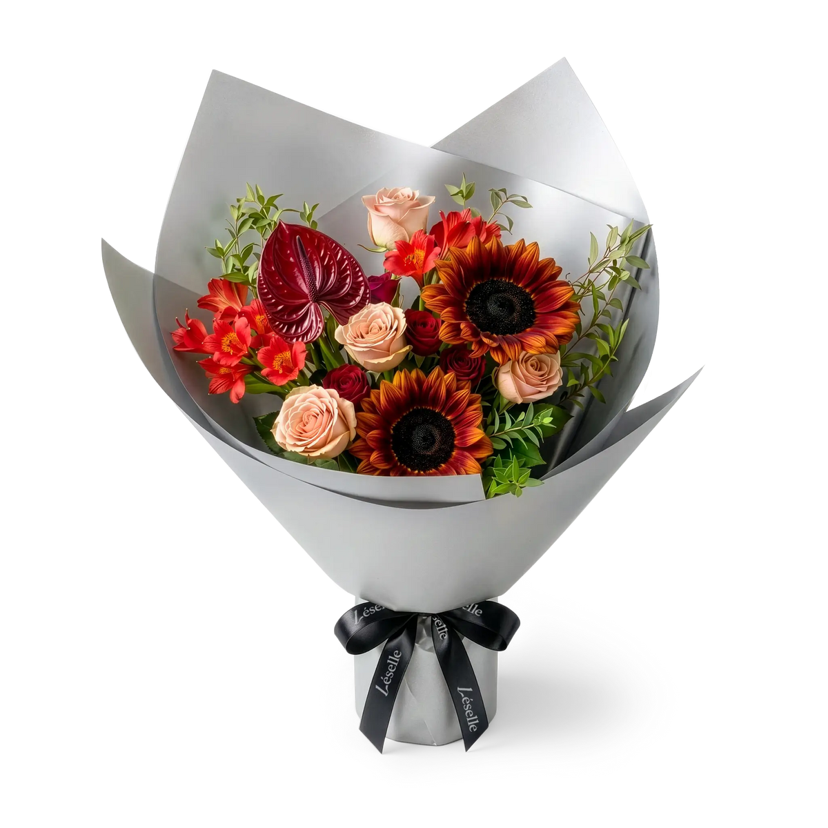 A wrapped flower bouquet featuring burgundy sunflowers, cappuccino roses, a dark red anthurium, and green foliage, wrapped in a silver paper sleeve with a black ribbon, on a transparent background.